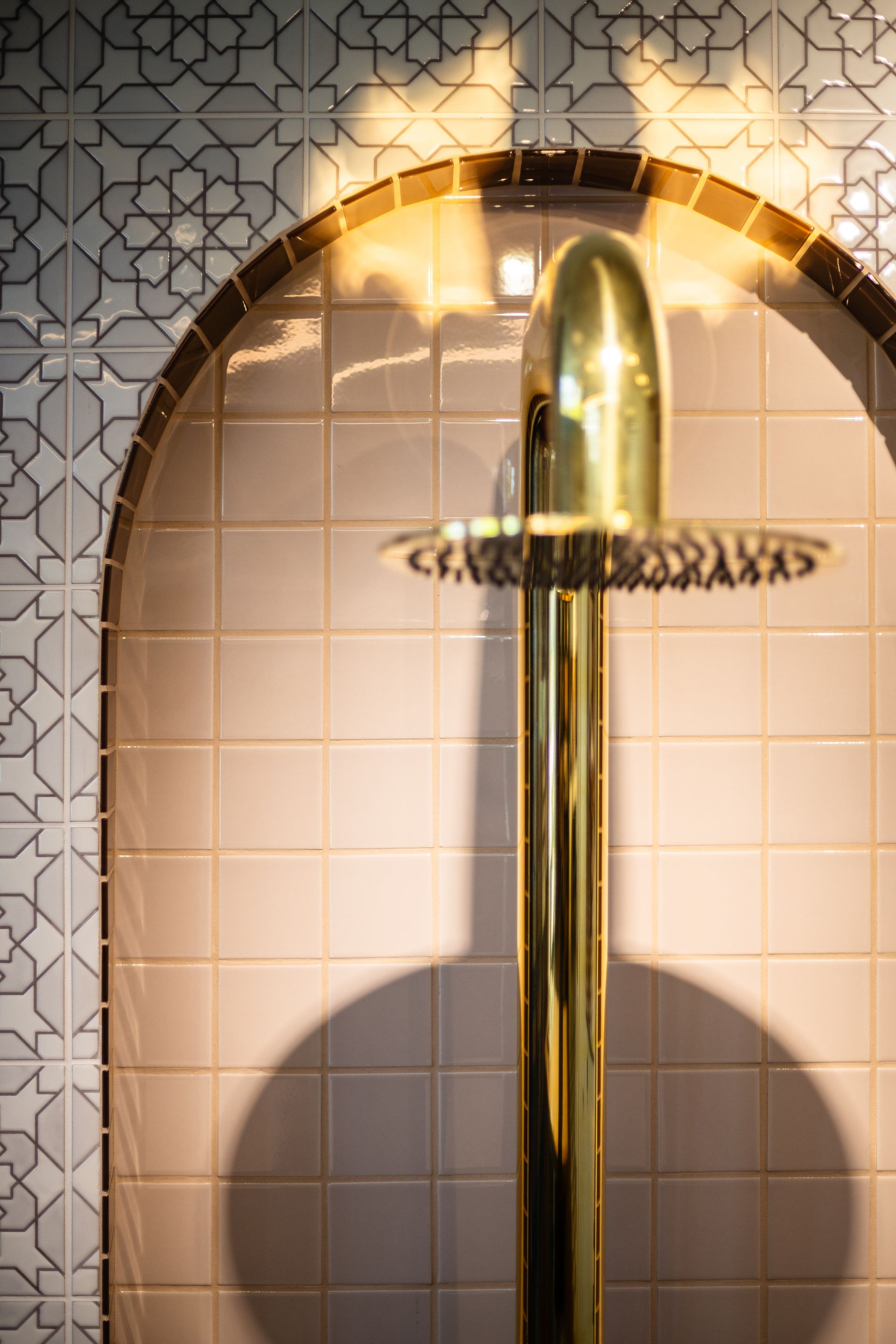 Polished chrome shower fixture against white tiled wall with patterned border
