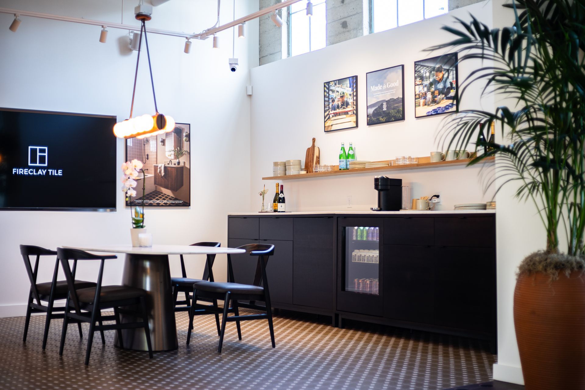 Modern café lounge with tables, black chairs, wall art, and a counter with plants and a coffee machine