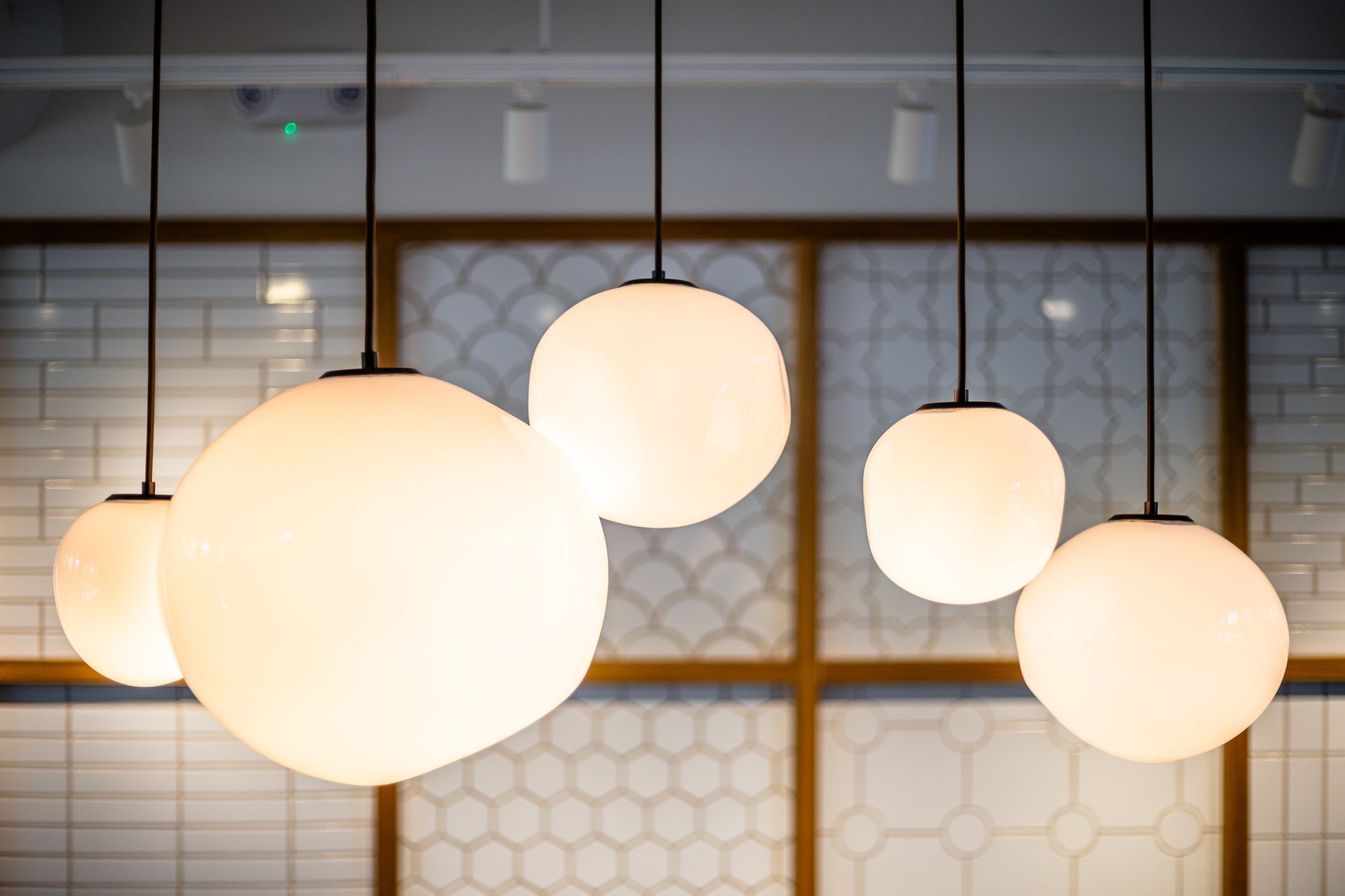 Five glowing round pendant lights hanging before a patterned wall and window grid.