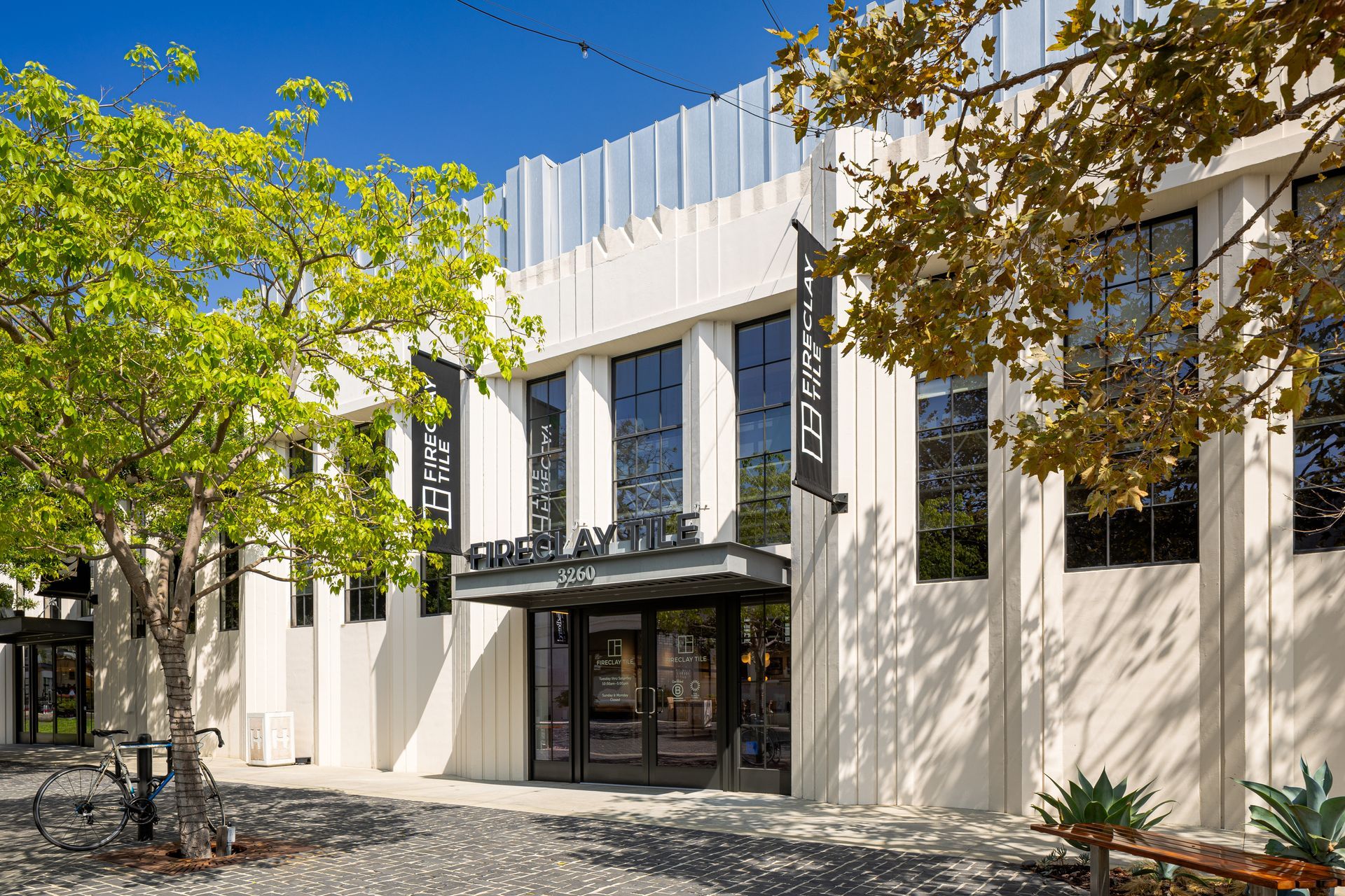 Modern white building with large windows and trees in front, under a clear blue sky