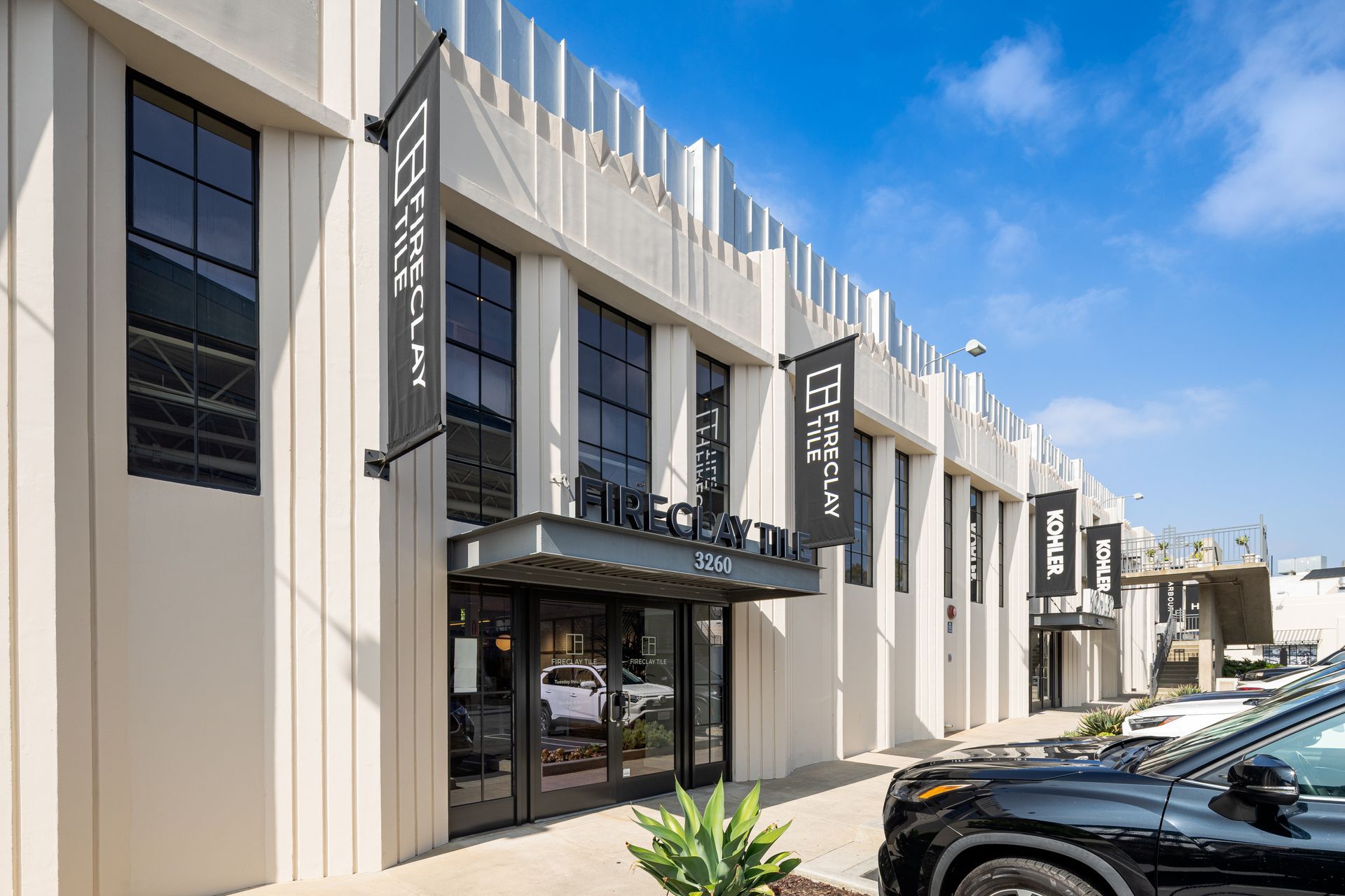 Modern beige storefront with black awnings and parked cars under a blue sky