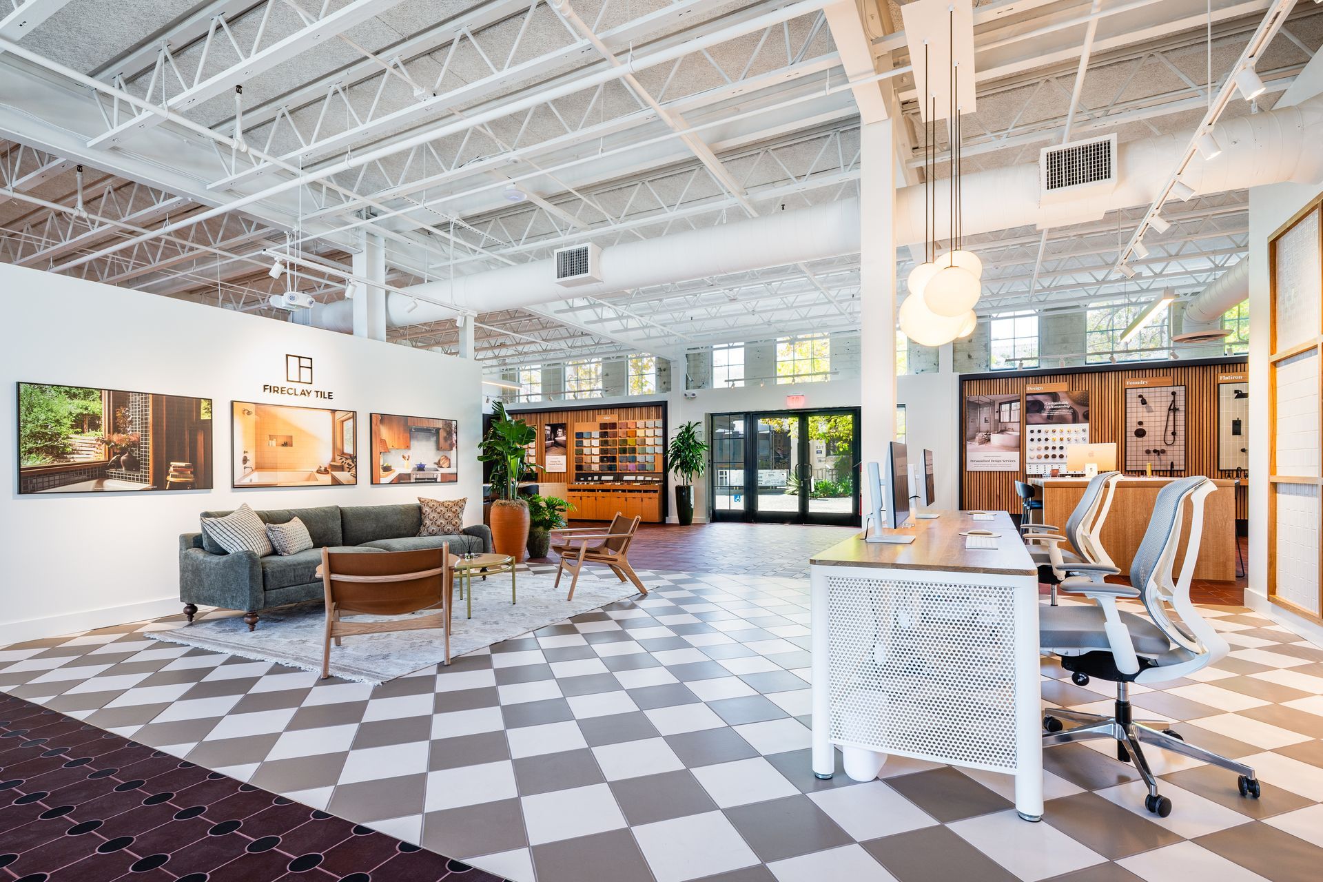 Bright modern office showroom with checkered floor, desks, chairs, and lounge seating under white ceiling beams