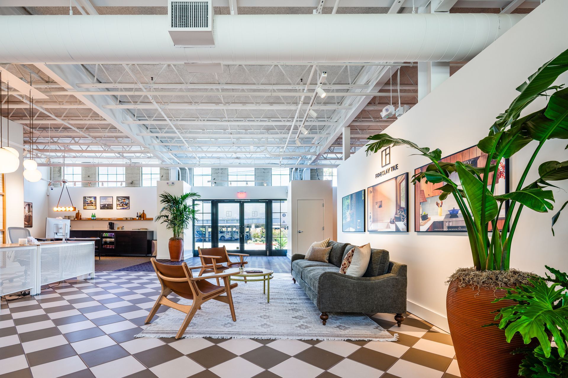 Bright modern office lounge with chairs, couch, front desk, and large potted plants on a checkered floor.