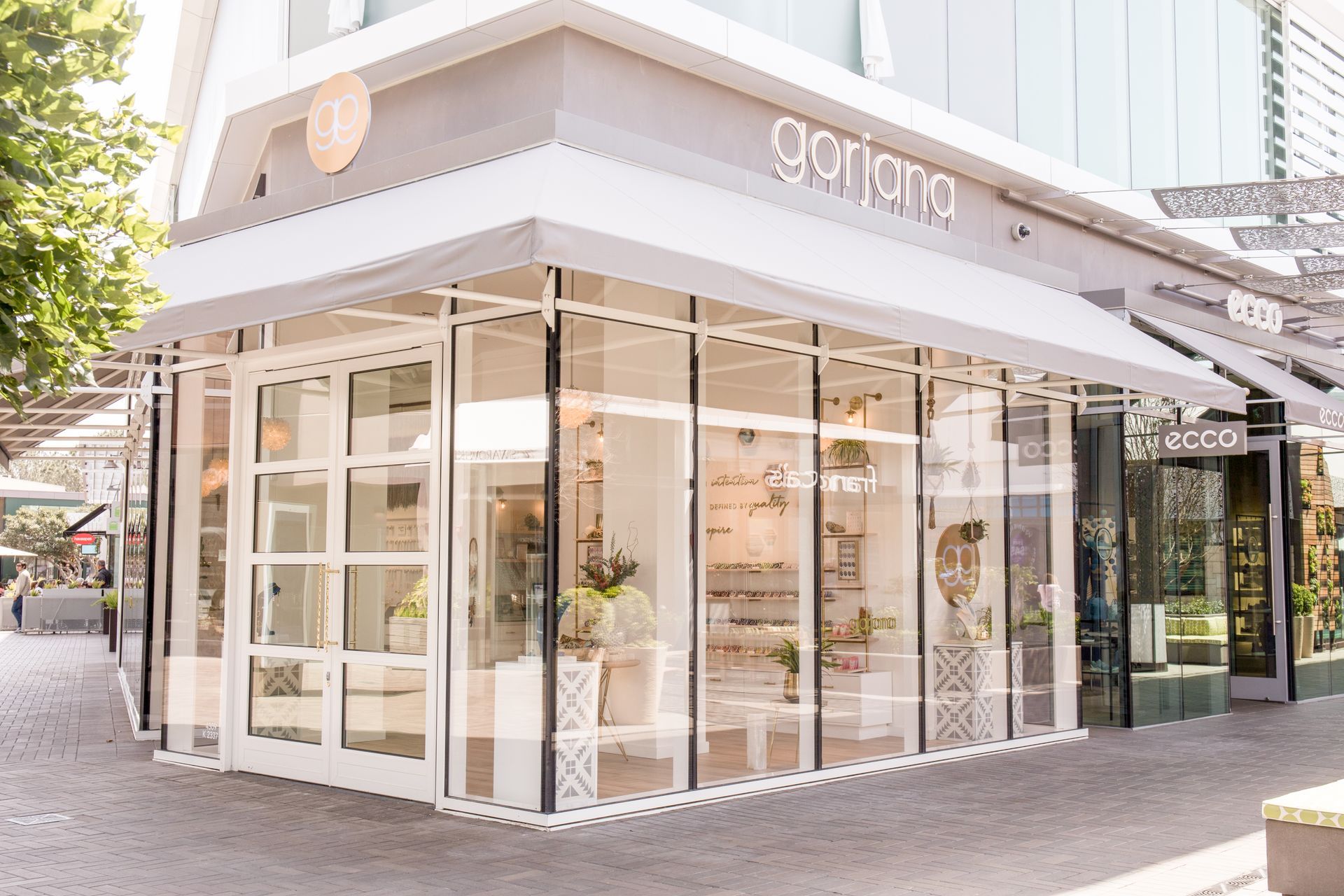 Corner storefront with white glass facade and beige awning on a pedestrian street.
