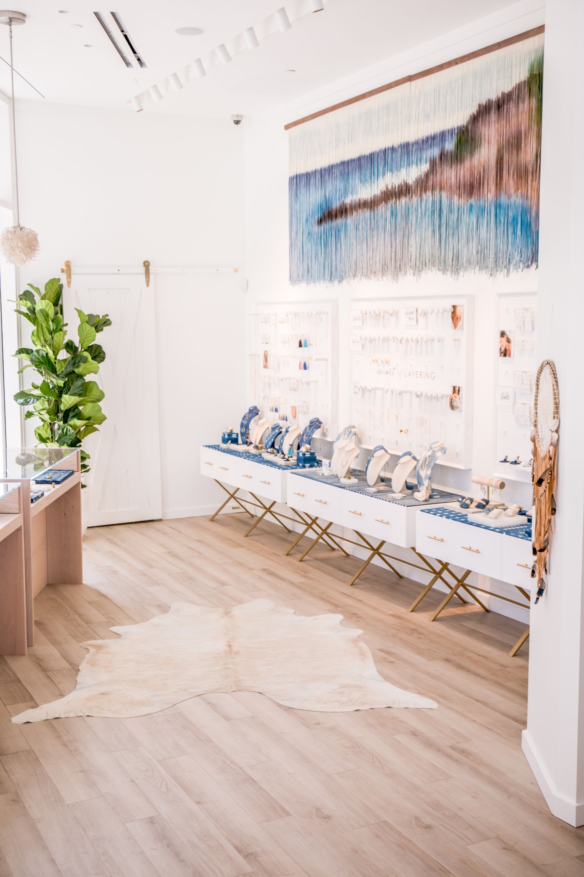 Bright, minimalist boutique with blue decor, wall art, display table, and a cowhide rug on wood flooring