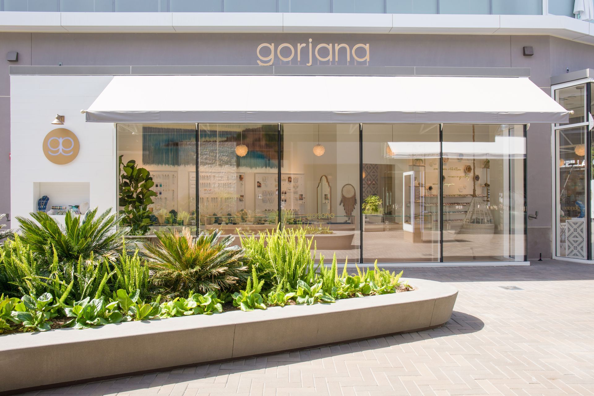 Modern storefront with glass windows, white awning, and landscaped greenery outside