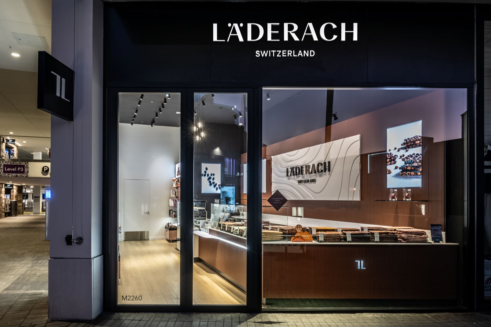 Laderach chocolate shop storefront at night with illuminated display windows and open entrance