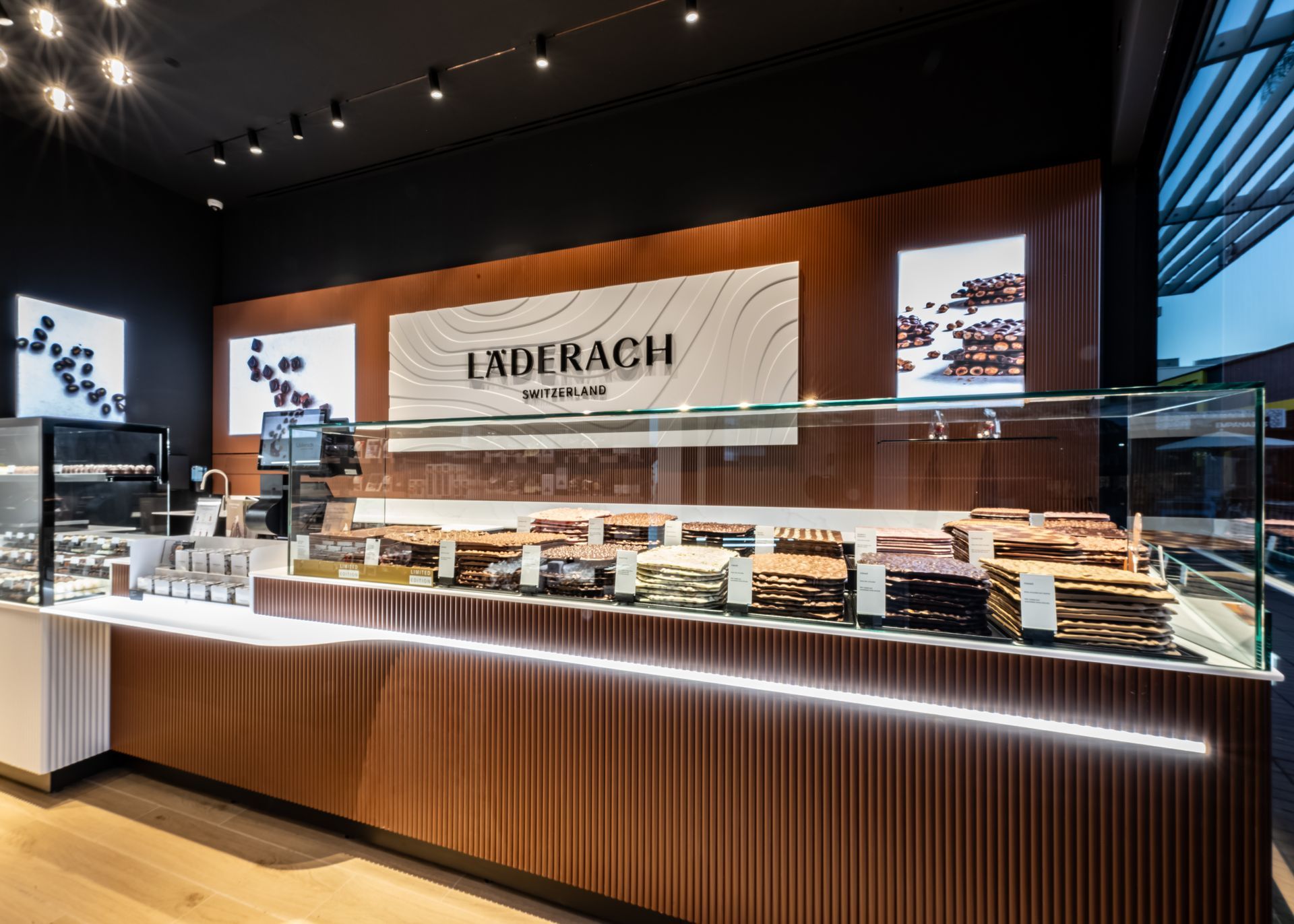 Modern bakery counter with pastries, wood paneling, and “Exderach” sign in a bright store interior