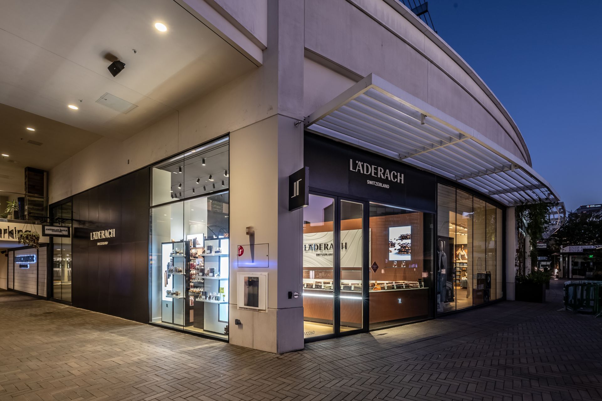 Modern storefront at dusk with illuminated glass windows and a curved awning in a shopping center