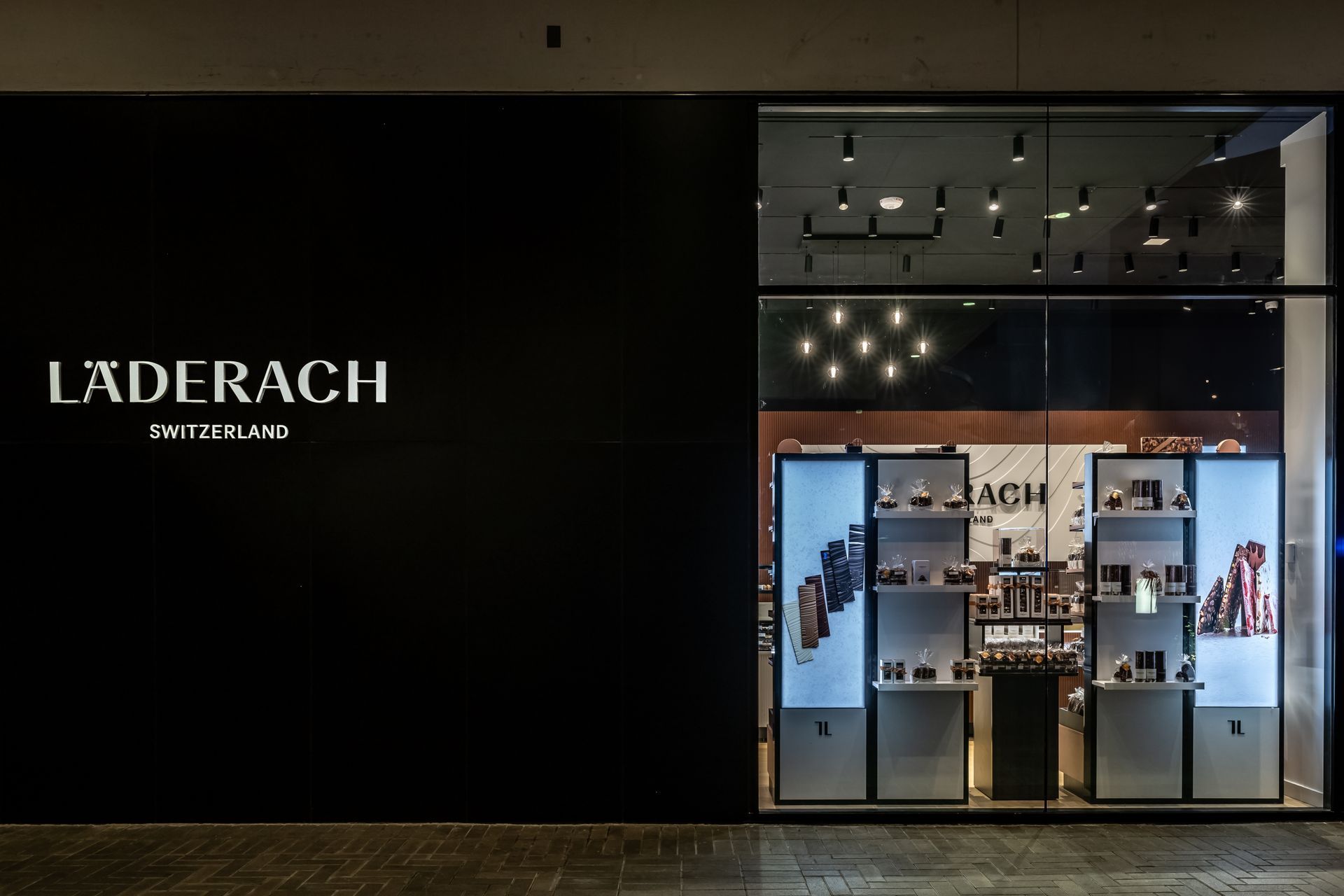 Läderach chocolate shop storefront with black facade and bright display windows in a mall corridor