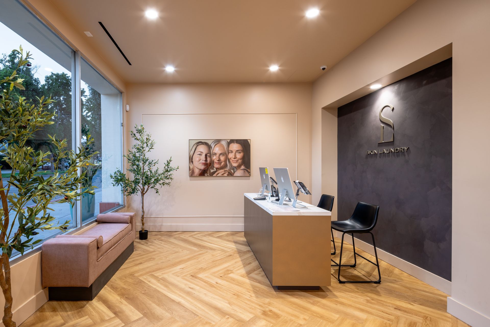 Modern office lobby with reception desk, black accent wall, bench by large window, and herringbone wood floor