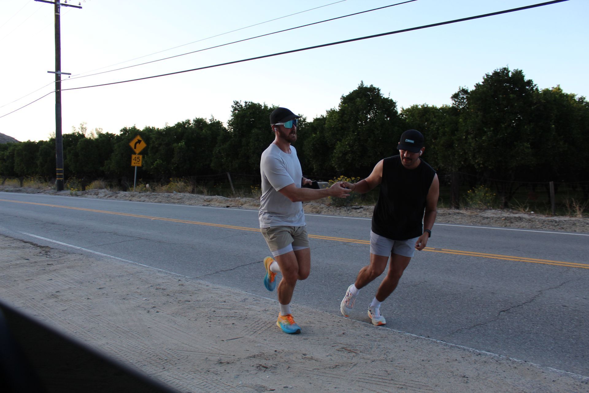 Two runners holding hands on a road at dusk, with trees and power lines in the background