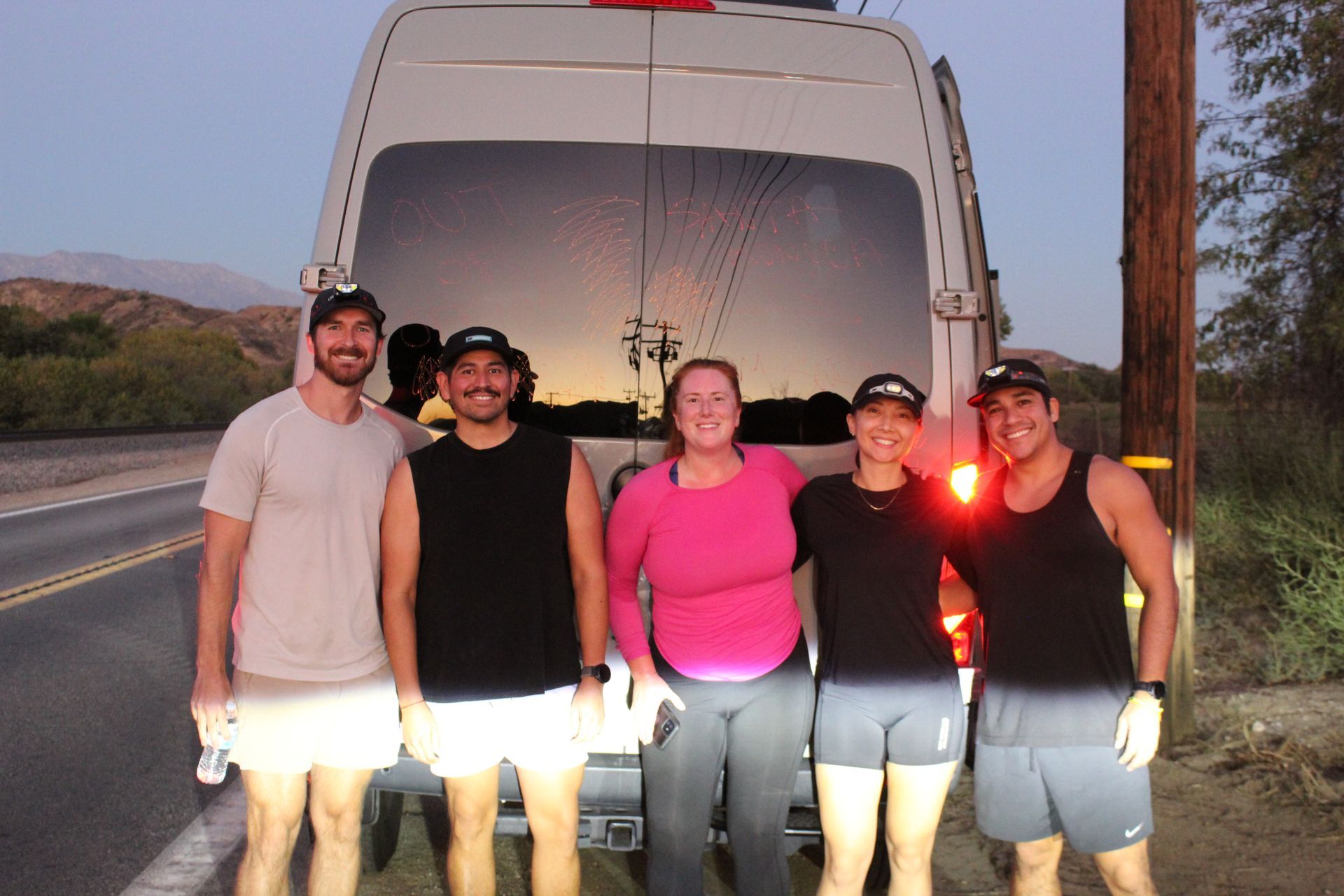 Five people standing in front of a white van at dusk on a roadside