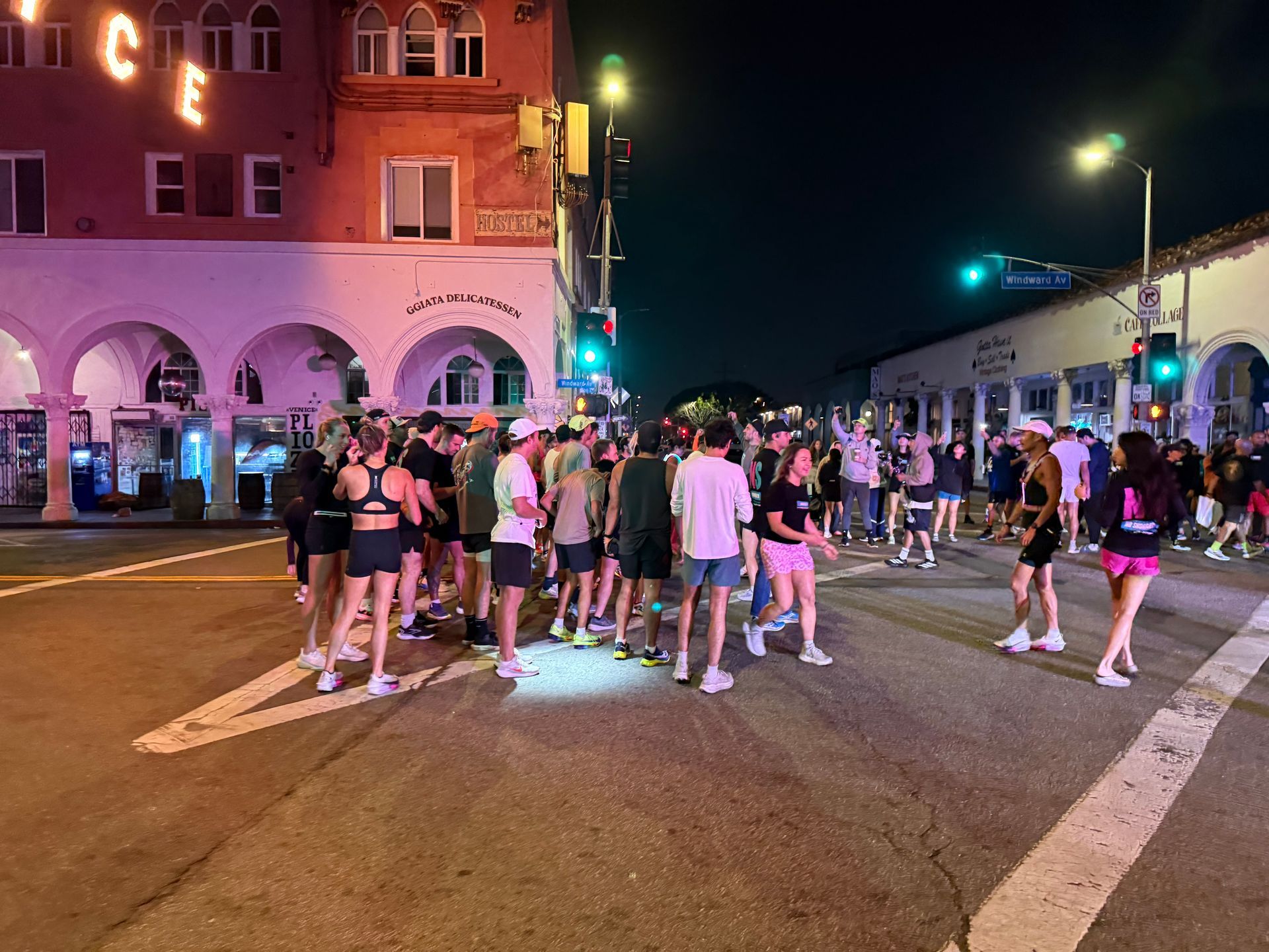 Crowd of people standing in a lit street at night near a corner building and storefronts