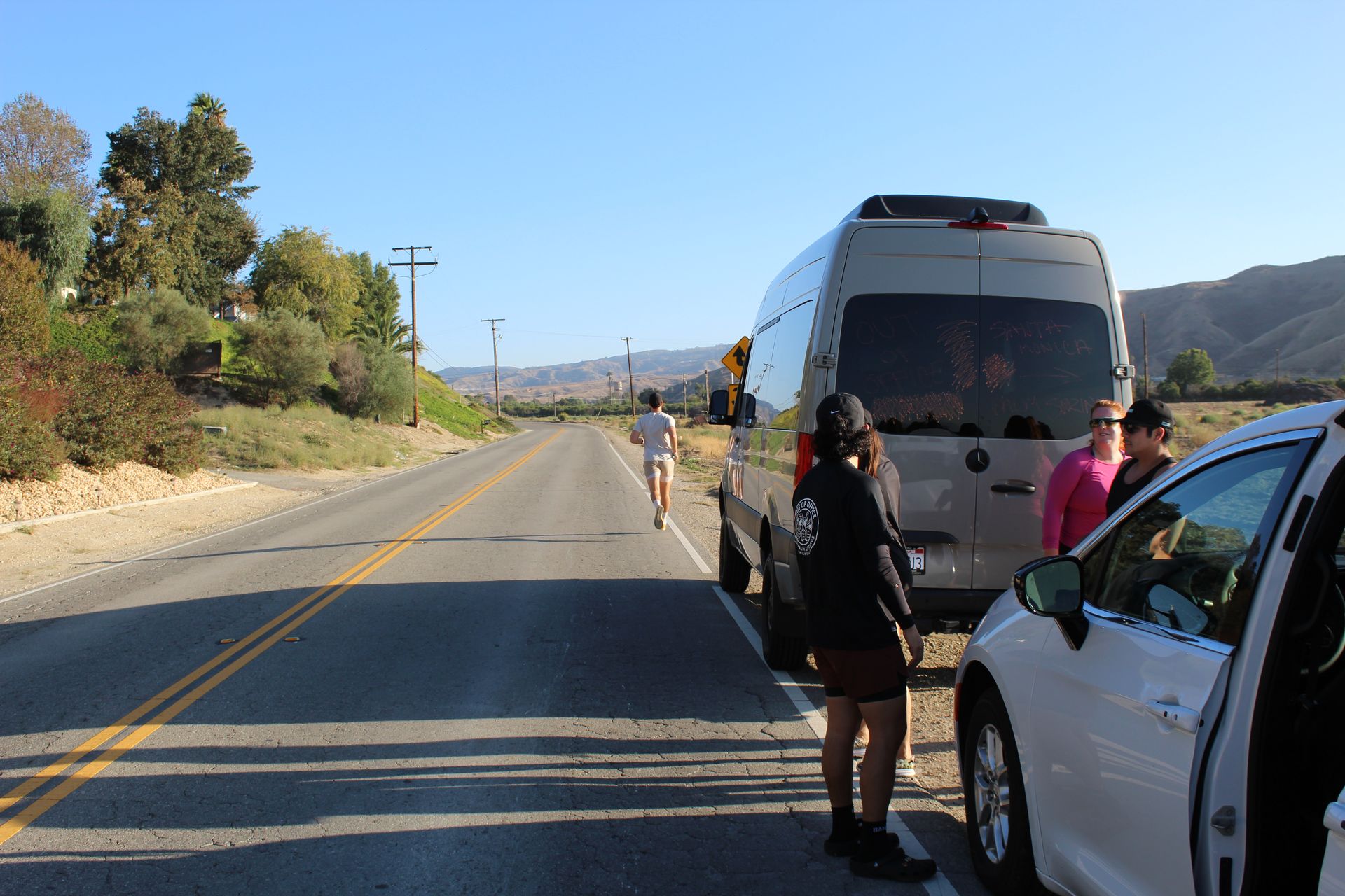 People standing by a white van on a rural road under a clear blue sky