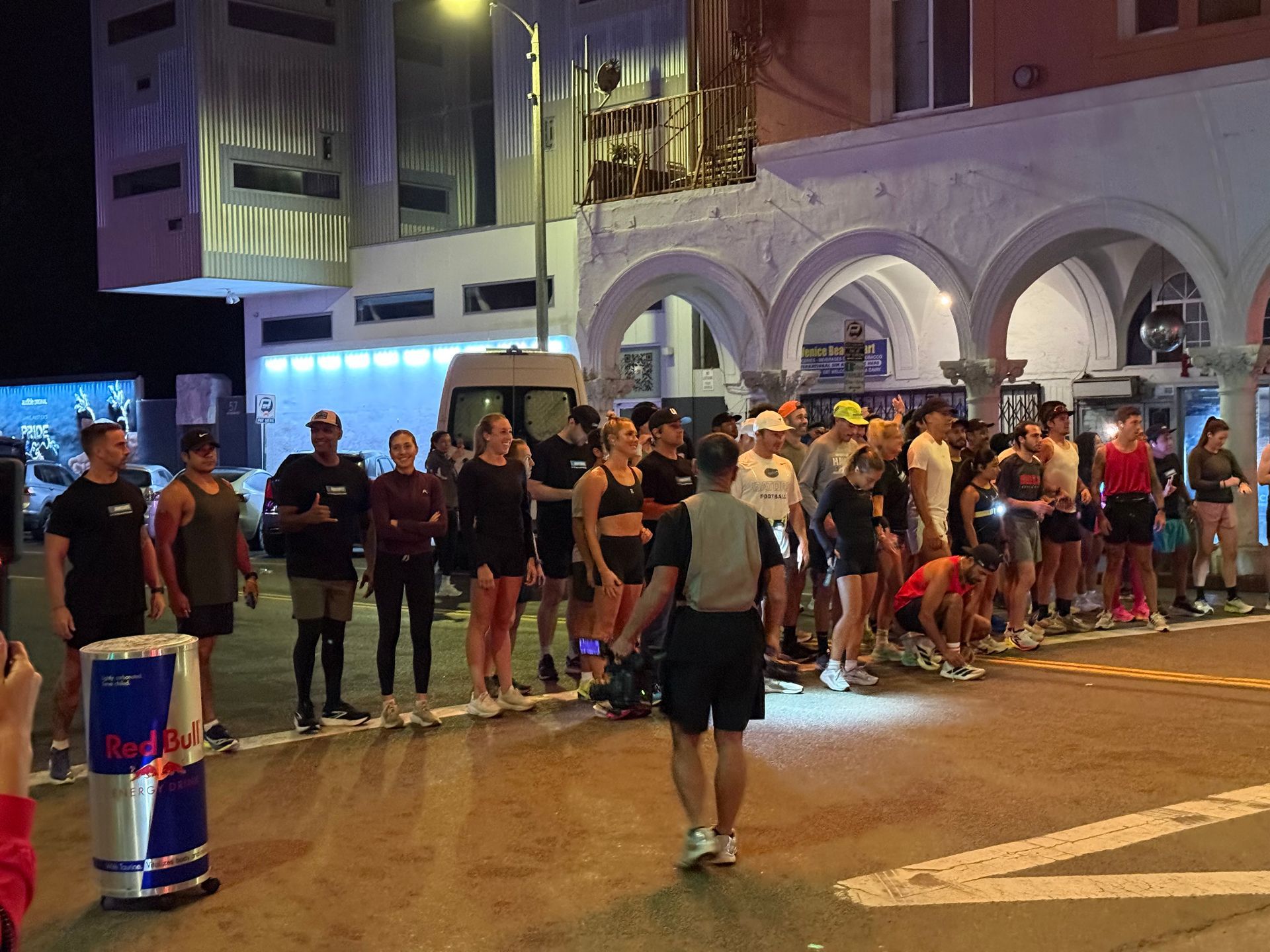 Crowd lined up at a nighttime street event outside a building with arches and blue lighting