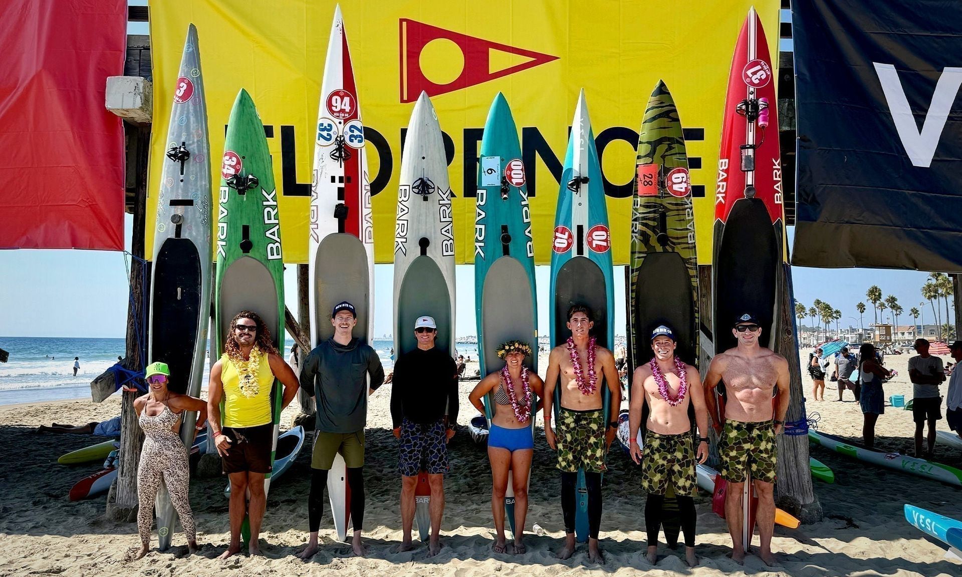 People standing before colorful surfboards and flags on a beach backdrop
