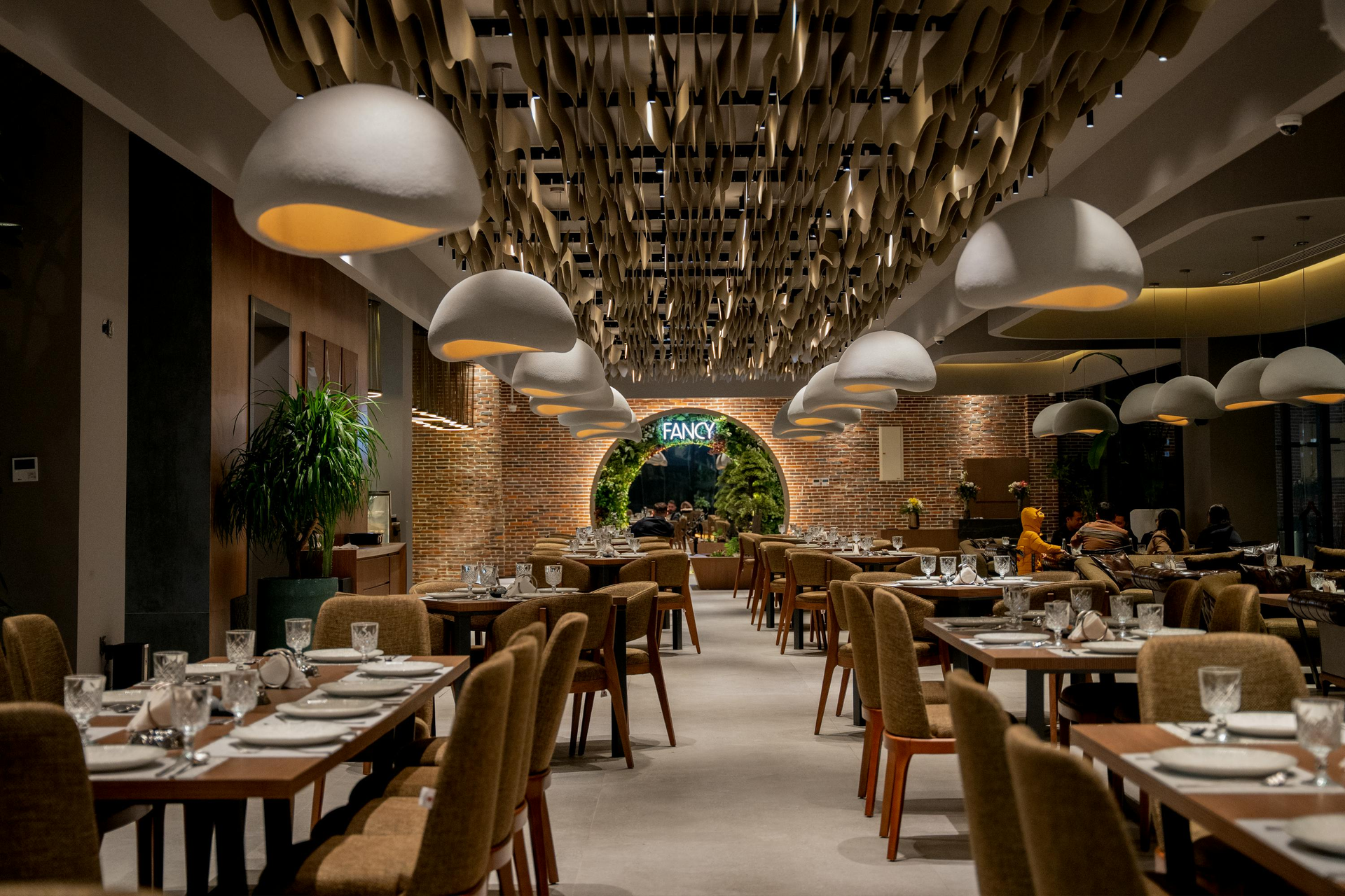 Elegant restaurant dining room with wooden tables, hanging lamps, and a brick archway at the back.