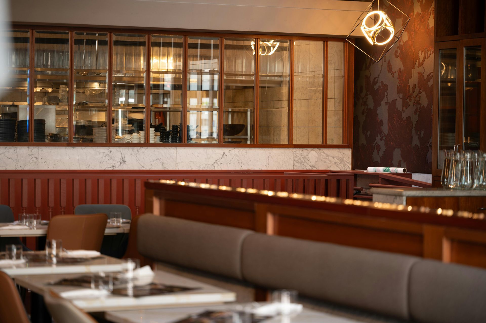 Warm-toned restaurant dining area with bar seating, tables, and shelves behind glass partitions