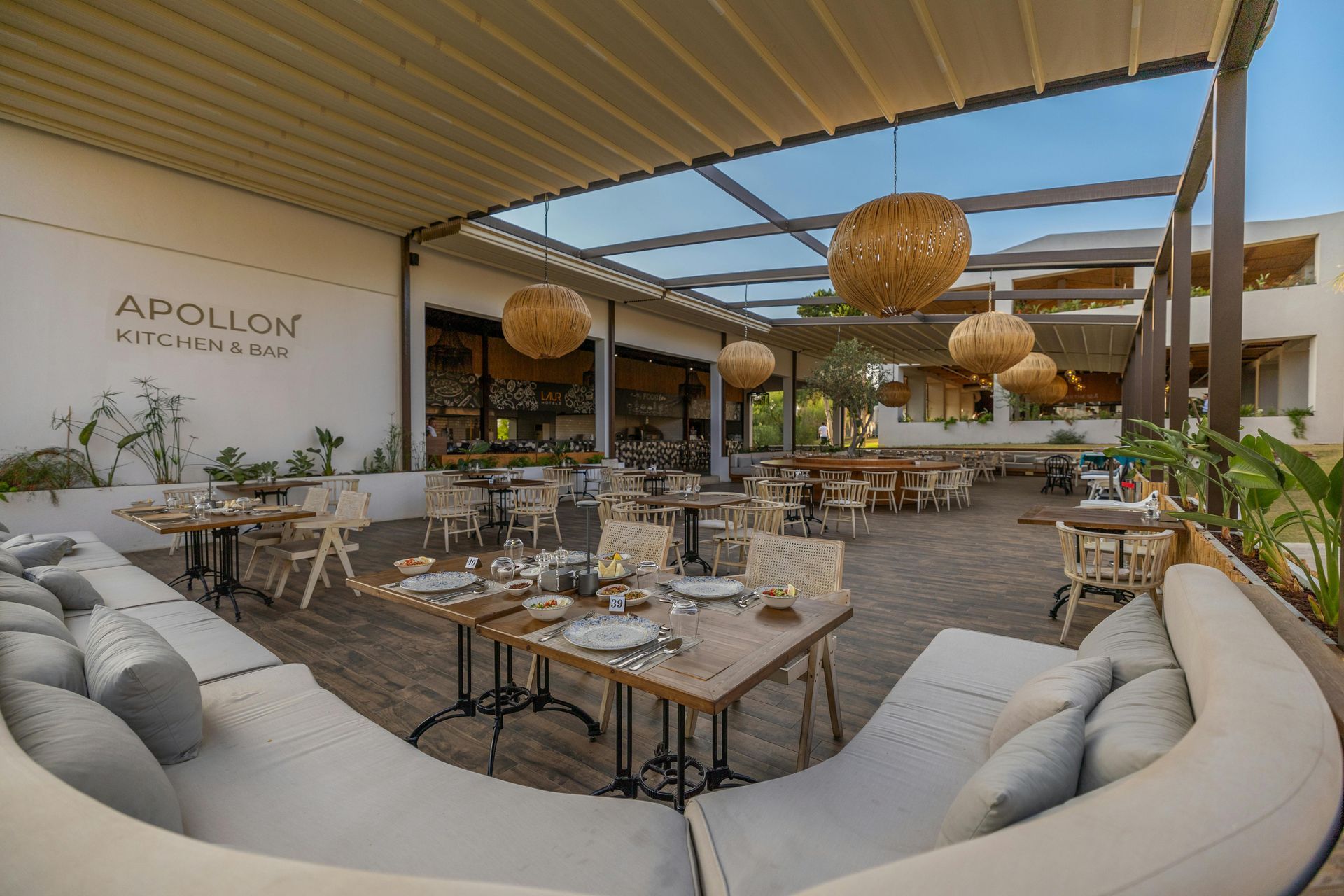 Outdoor restaurant patio with wicker chairs, tables, and hanging lanterns under a shaded pergola