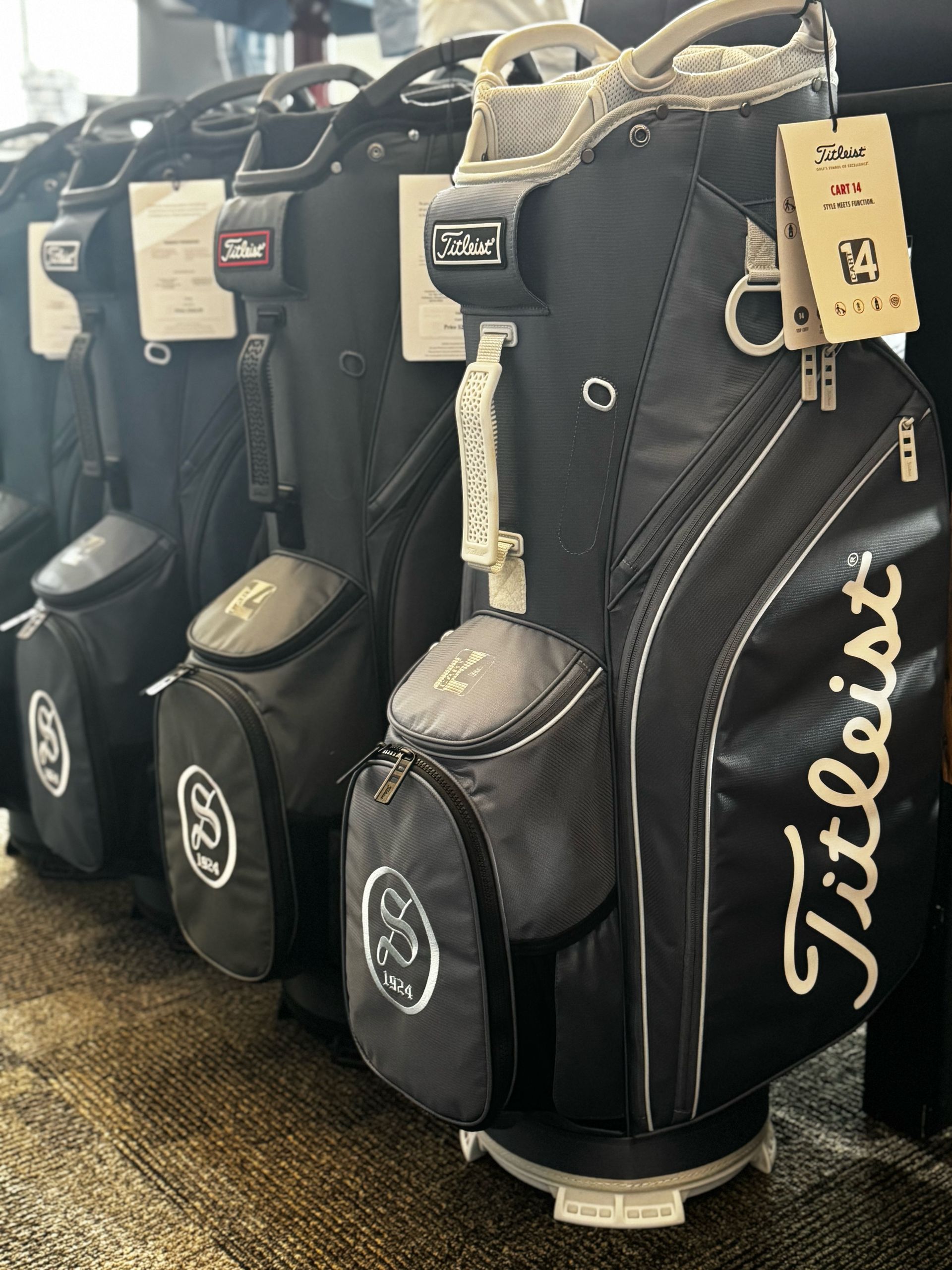 Black Titleist golf bags lined up in a store, with white logos and tags attached.