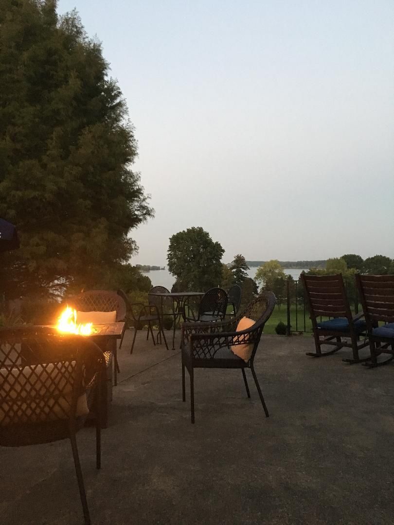 Outdoor seating area at dusk with a small fire burning in a metal basket and empty chairs nearby