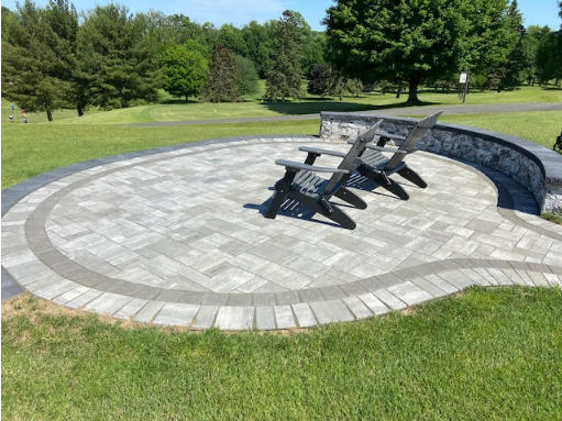 Curved stone amphitheater seating in a grassy park with several wooden benches in the center