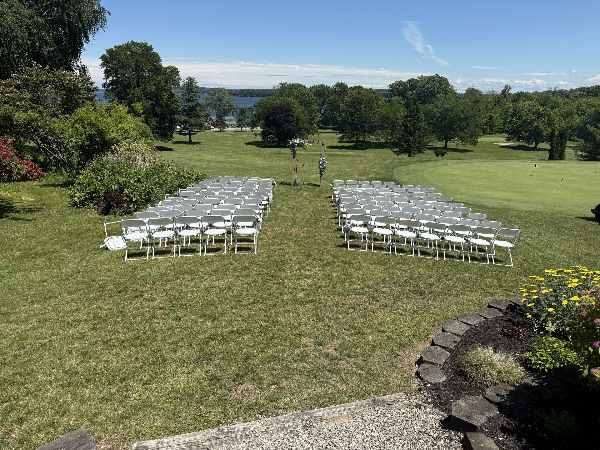 Bride and groom stand on a green golf course under a bright sky, with sand traps behind them.