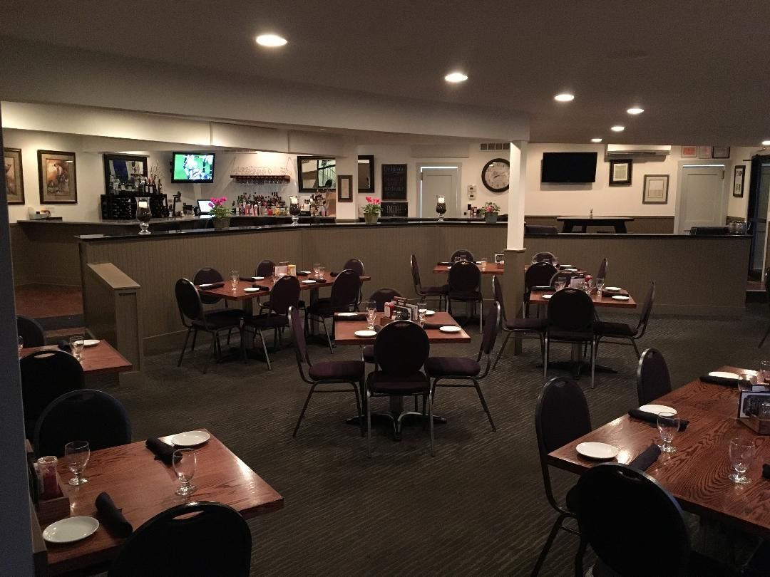 Empty restaurant dining area with tables and chairs, softly lit bar in the background