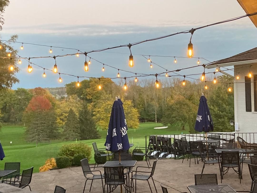 Patio with string lights, tables, umbrellas, and a scenic garden view at sunset