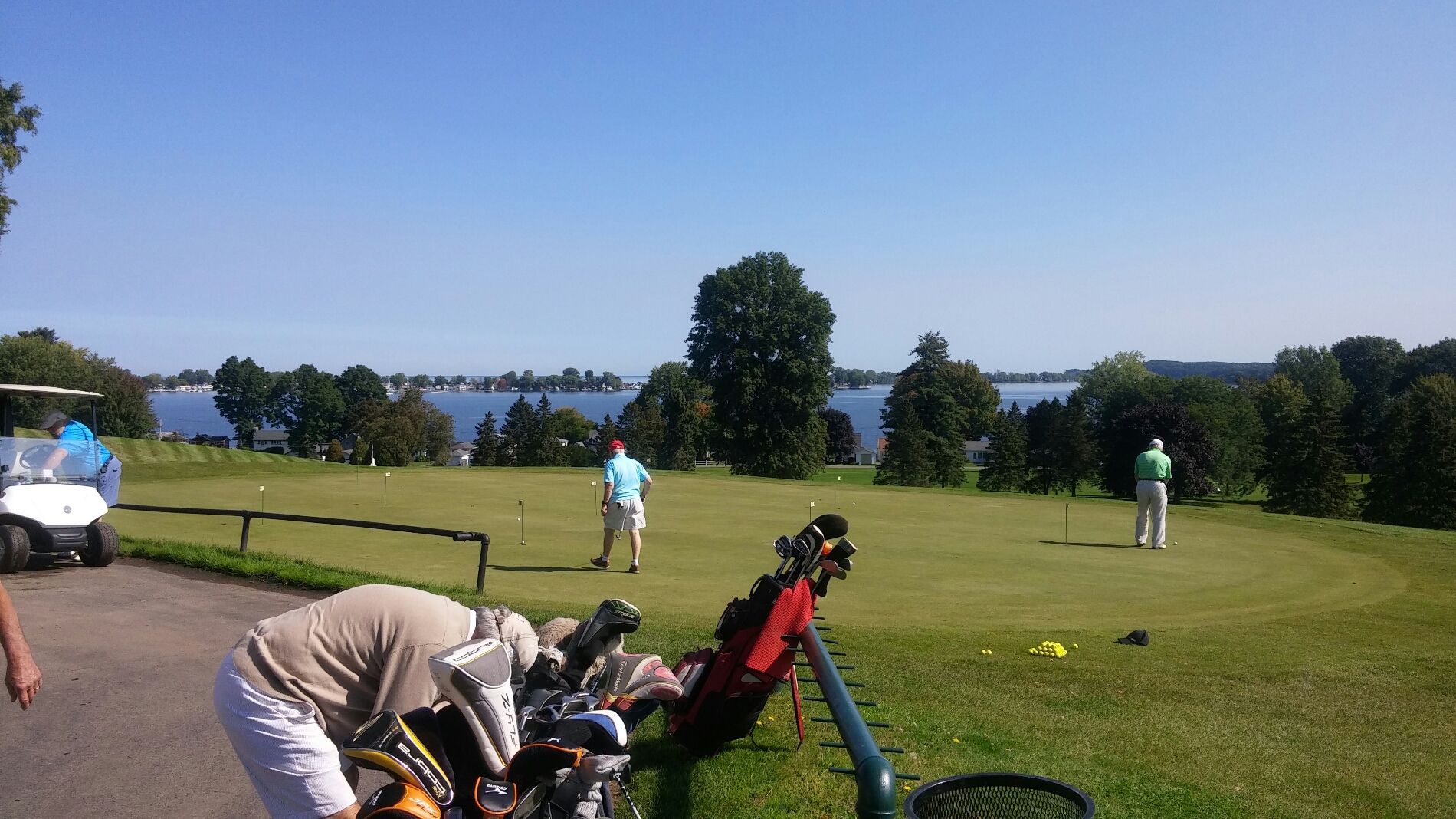 Golfers on a sunny course near water, with golf bags in the foreground.