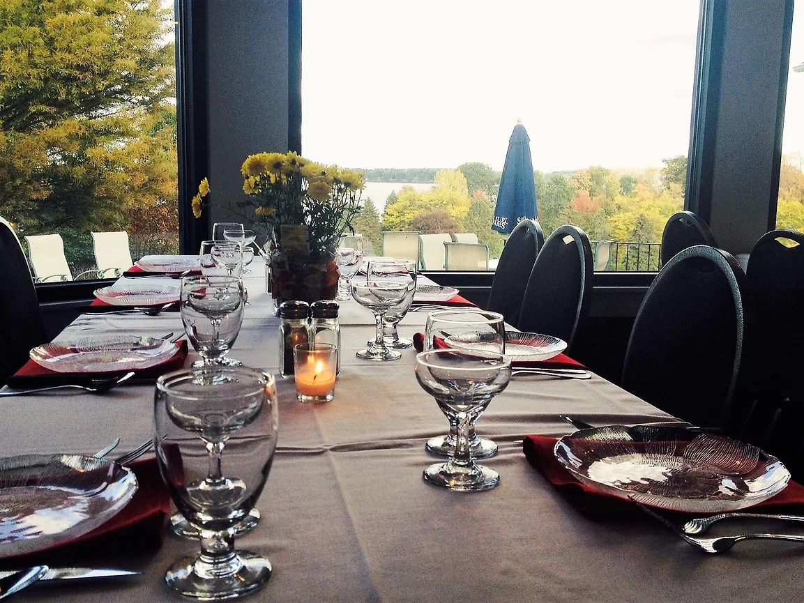Elegant dining table set for a meal, with red plates, glassware, candles, and a countryside view beyond large windows