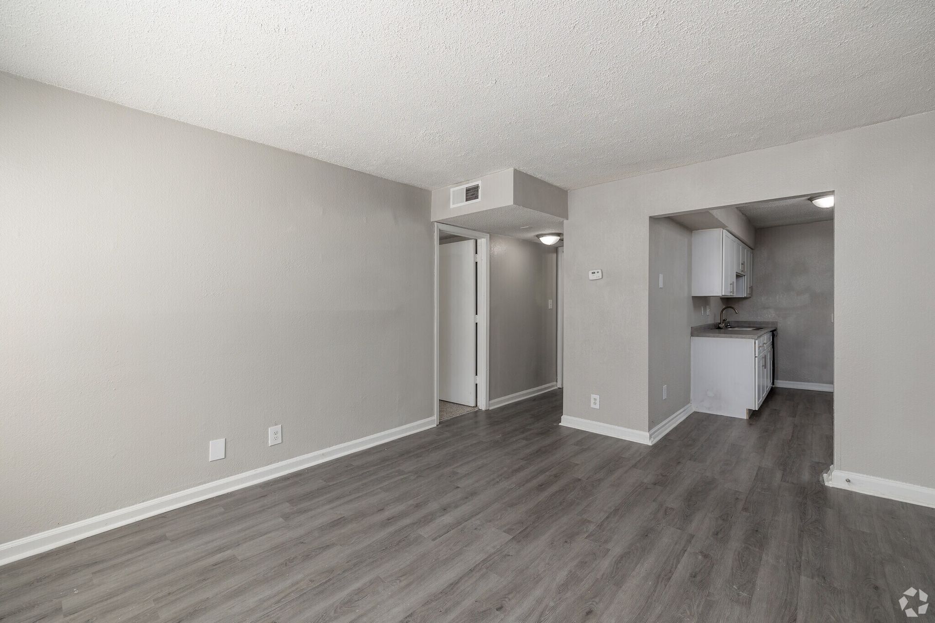 Photo of a living room with the kitchen in the background, as well as the hallway and entrance to another room
