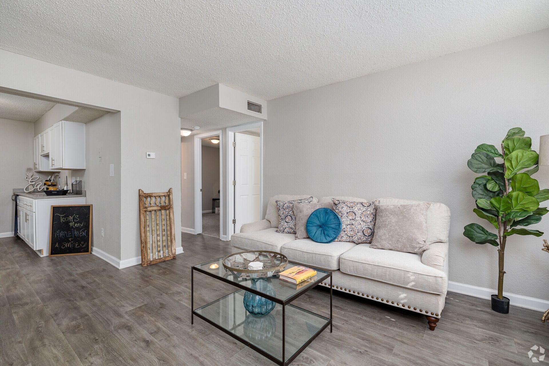 Photo of a living room with the kitchen and hallway in the background