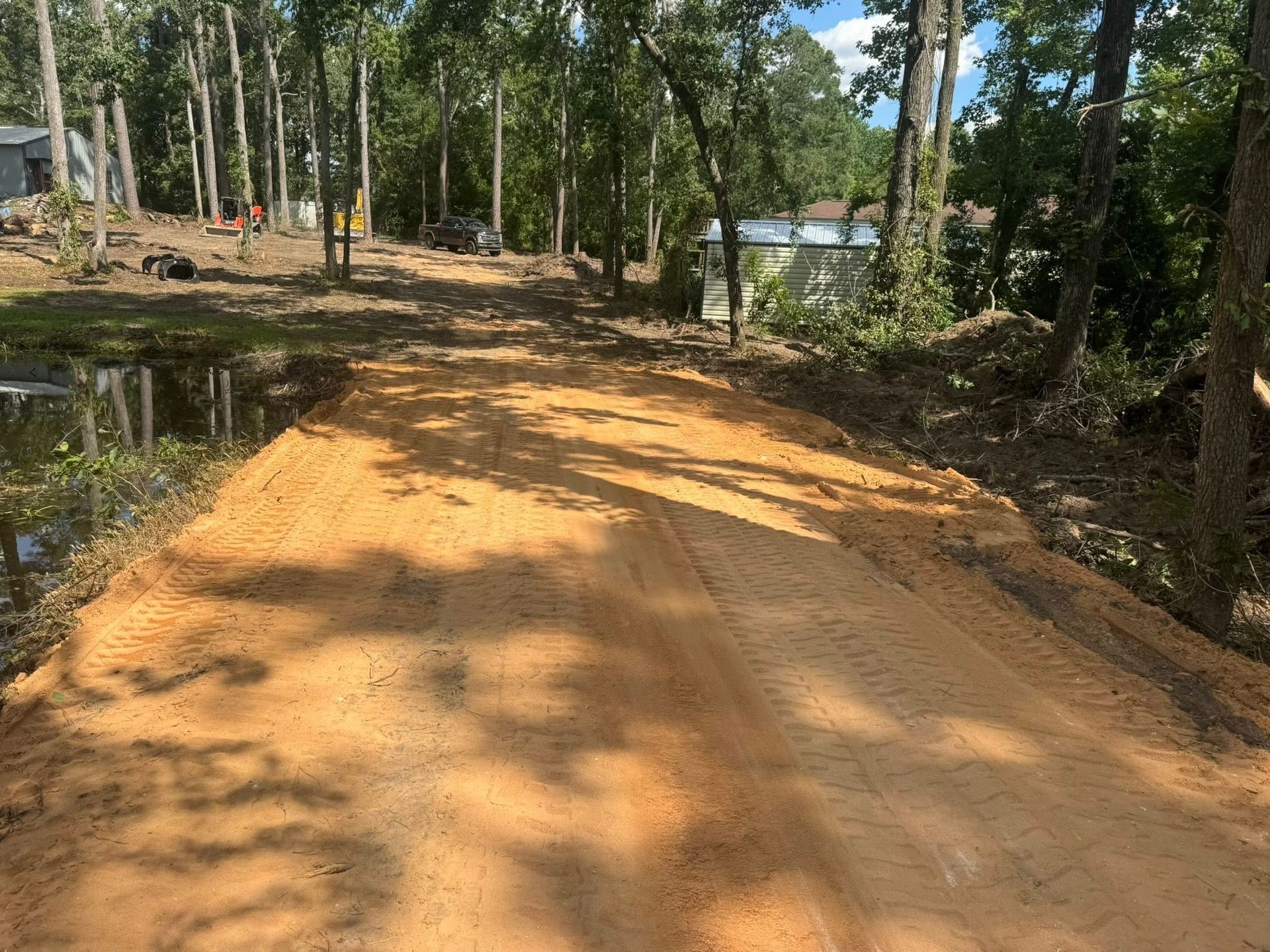 Dirt road through a wooded area, freshly graded with light-brown soil.