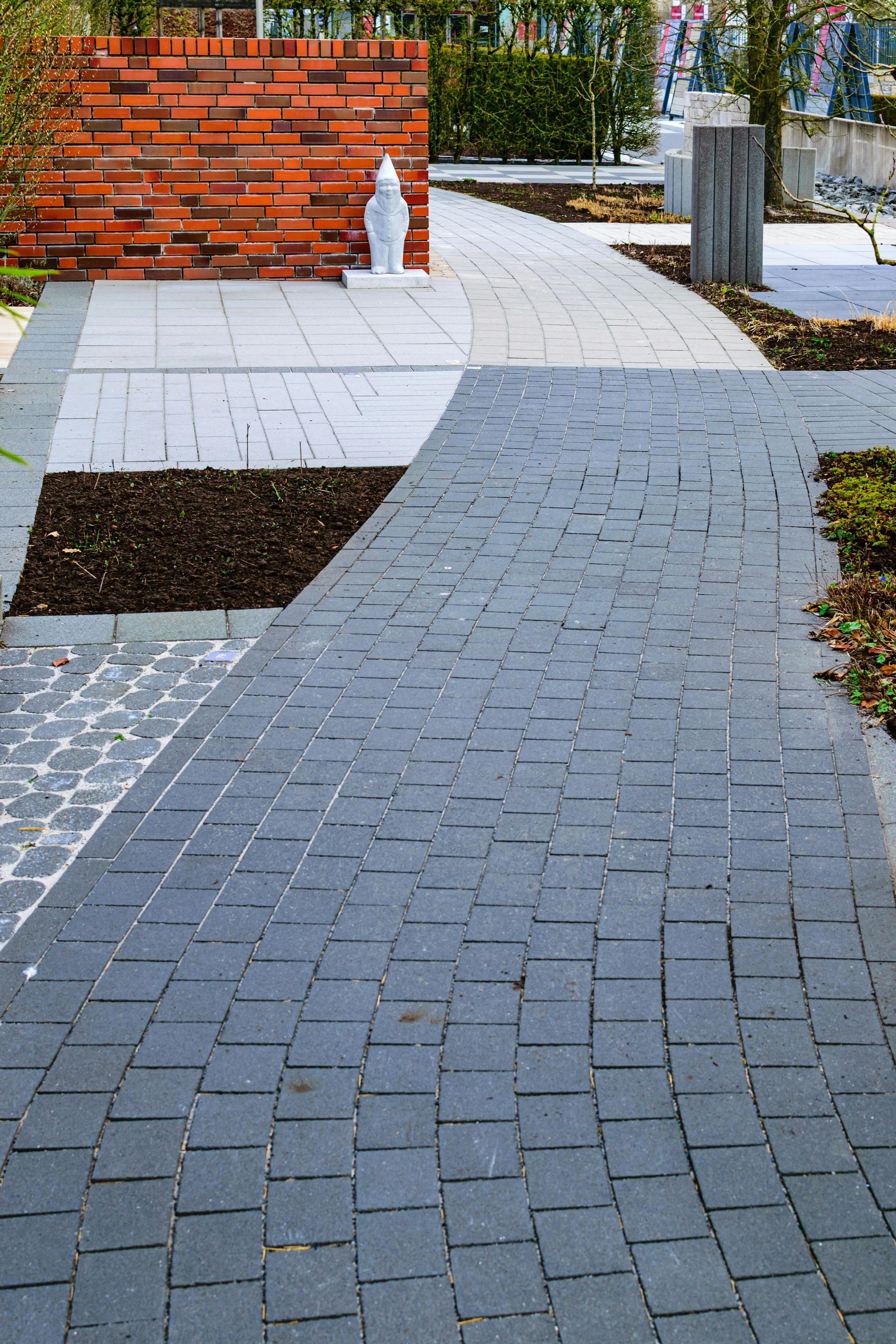 Neatly trimmed hedge beside a gravel garden path, with a house and lush greenery in the background