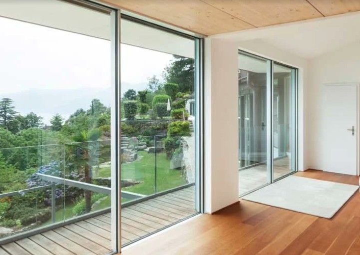 Interni moderni con grandi porte a vetri che si affacciano su un rigoglioso giardino e pavimento in legno con tappeto bianco.