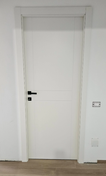 Porta interna bianca con maniglia nera contro una parete bianca e finiture coordinate.