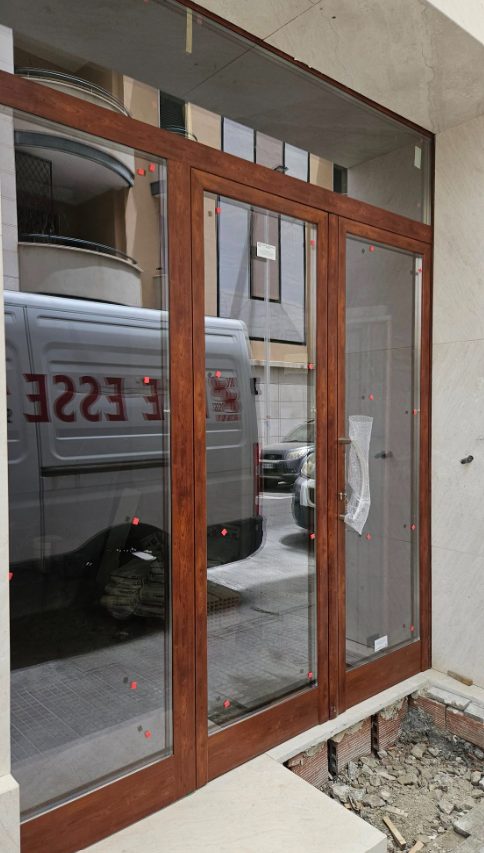 Porte e finestre in vetro con cornice in legno, che riflettono la scena della strada e un furgone bianco.
