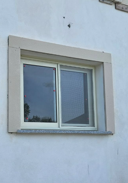 Finestra con telaio e davanzale color marrone chiaro su un edificio esterno bianco.