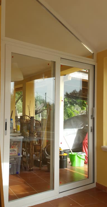 Porte scorrevoli in vetro con cornice bianca; vista sul patio esterno con oggetti, luce solare.