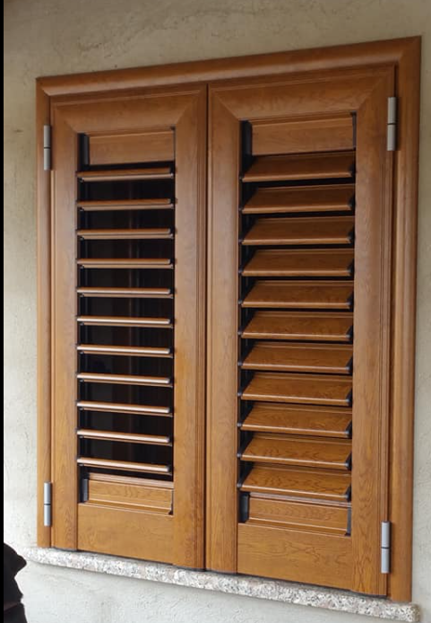 Persiane in legno marrone, chiuse, con stecche angolate. Cerniere visibili.