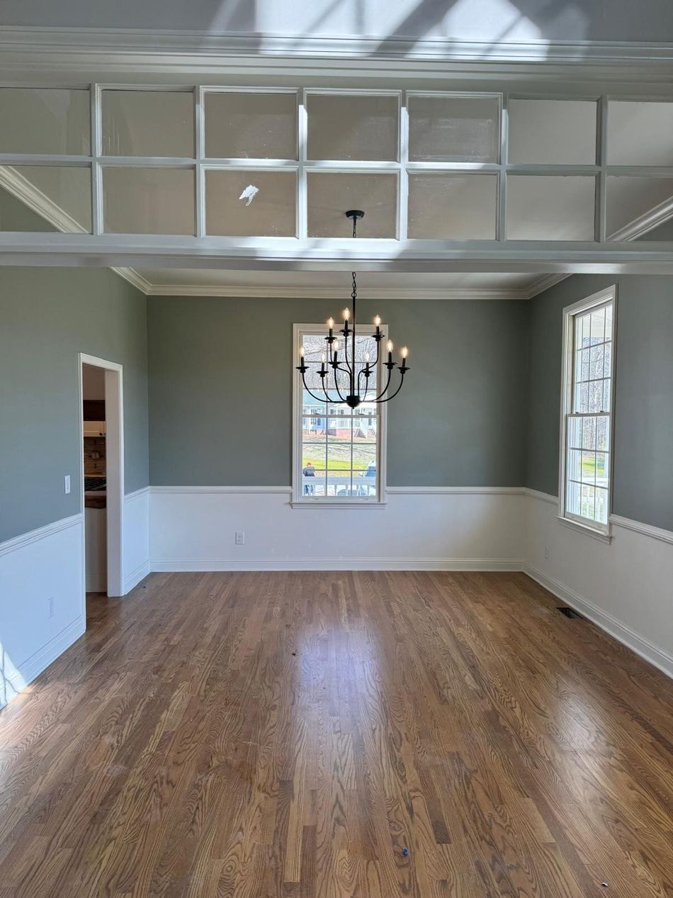 Empty dining room with hardwood floors, gray walls, white trim, chandelier, and tall windows.