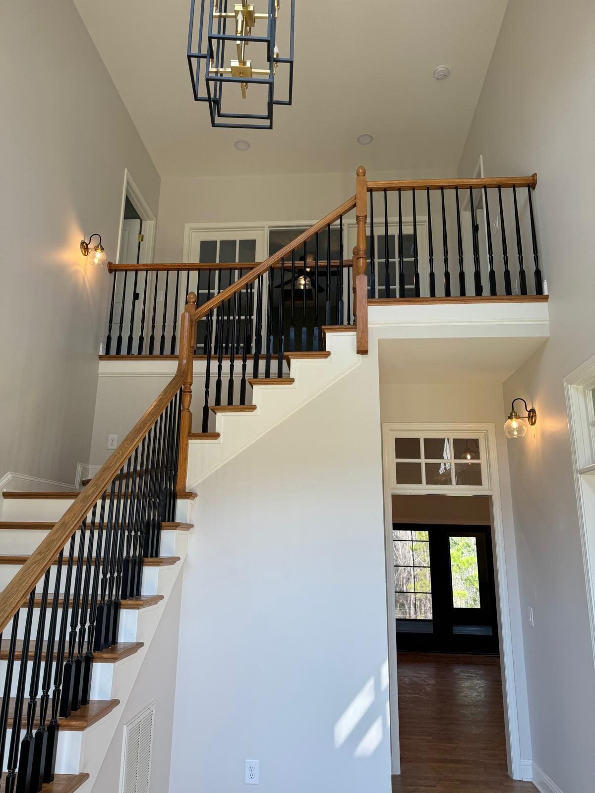 Tall foyer with a winding staircase, black balusters, white walls, and a hanging light fixture