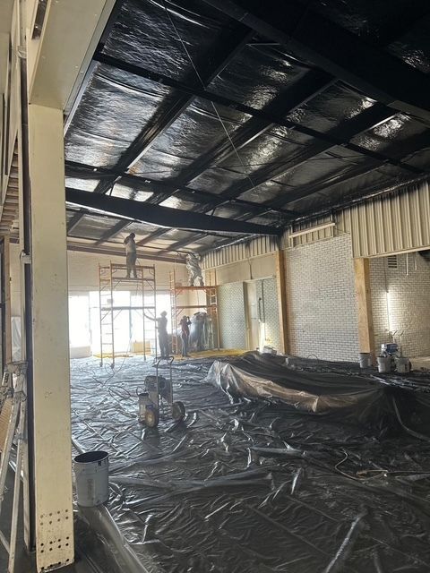 Interior of a construction site with a black tarp-covered floor and exposed ceiling beams under renovation