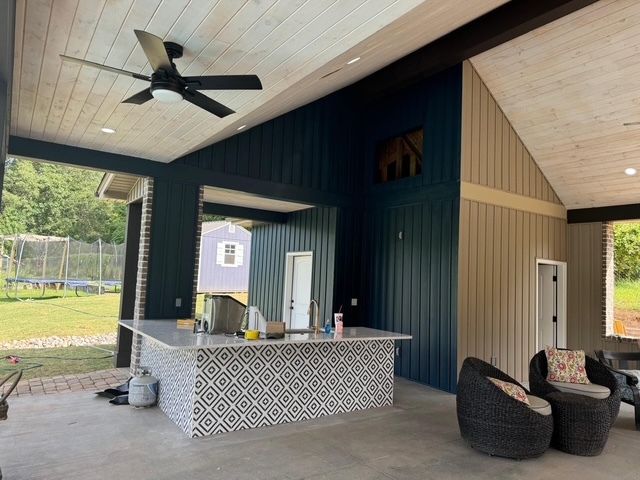 Covered outdoor patio with a bar, black ceiling fan, wicker chairs, and dark blue and tan walls