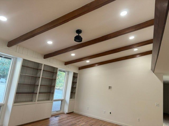 Bright room with vaulted ceiling, exposed beams, built-in shelves, and a doorway to outside.