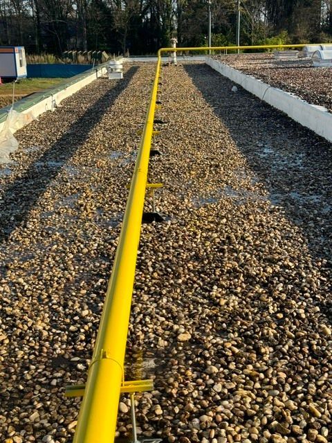 Yellow pipe running down a gravel drainage bed, viewed from above in an outdoor industrial area