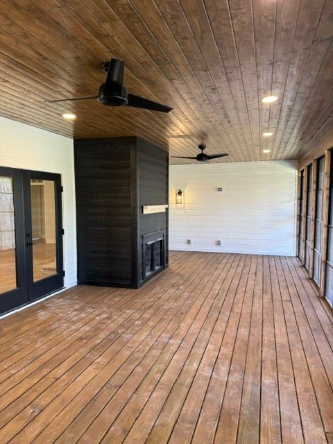 Spacious room with wood plank floors and ceiling, dark beams, fireplace, ceiling fans, and white paneled wall.