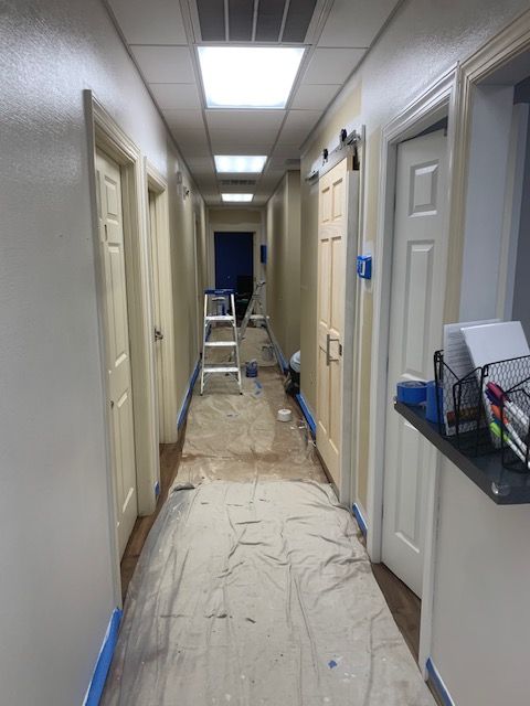 Narrow hallway under renovation with ladders, covered floor, and doors on both sides.